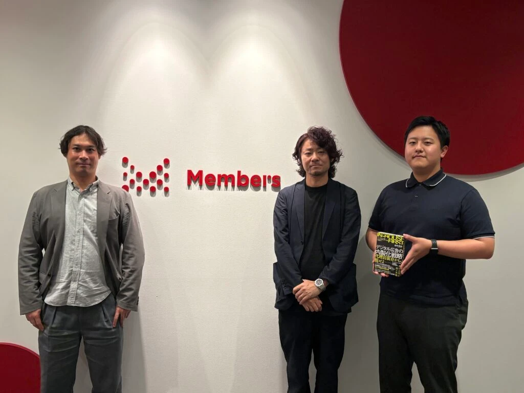 壁面のメンバーズロゴの前で並び立つ仲山氏（写真左）と田中（写真中央）、多田（写真右）